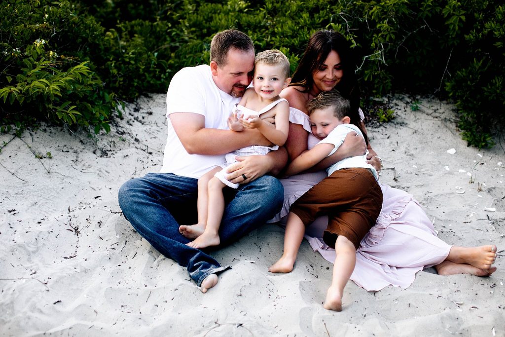 Family of four with two boys snuggling on the beach and laughing