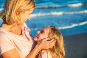 Daughter hugging her mother as a mother holds daughters face on the beach in Ocean City New Jersey