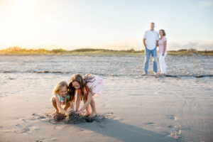 Parents watching in the distance as their daughters play in the sand at sunset on the beach in Ocean City New Jersey