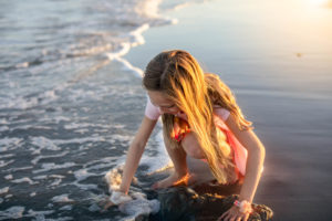 young girl kneeling down at the edge of the ocean