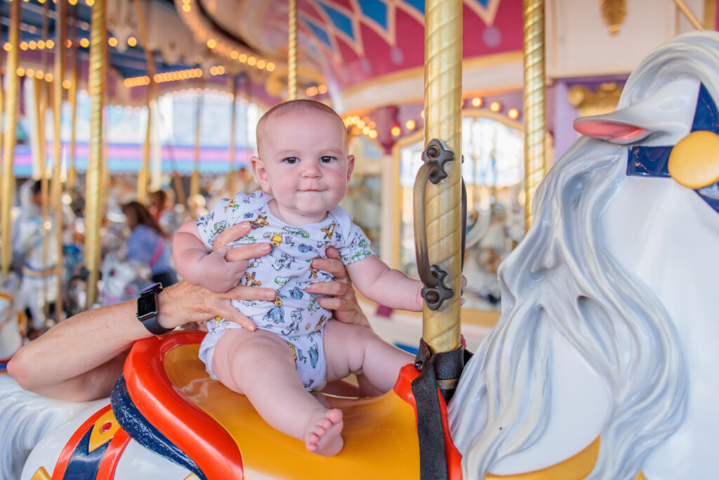 Baby sitting on a Carousel horse in Magic Kingdom at Walt Disney World Florida wearing a Winnie the Pooh Onesie